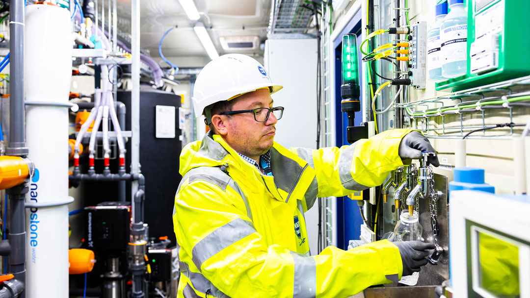 Man in PPE filling plastic bottle for testing