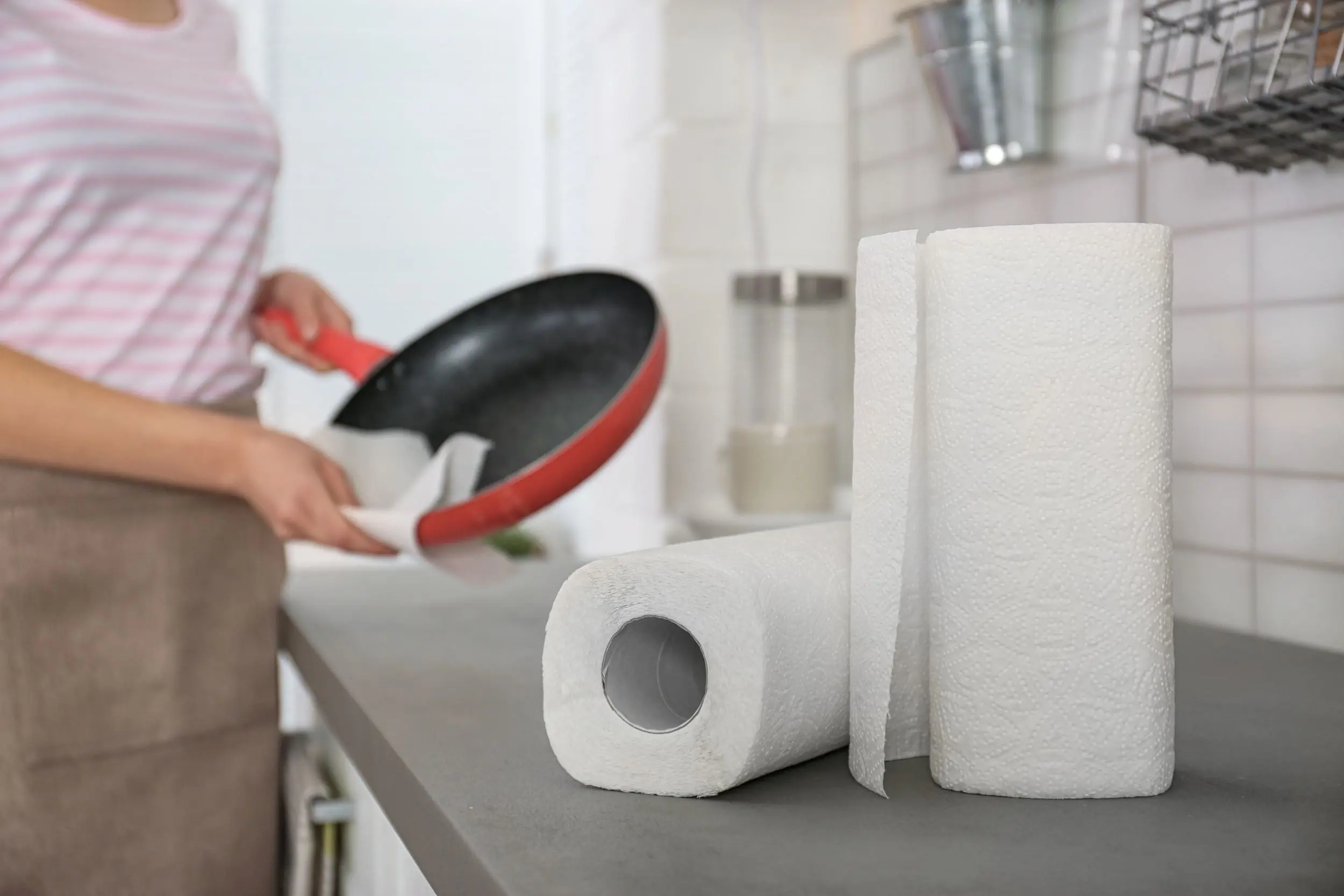 Using kitchen roll to soak up excess grease and oil from a frying pan