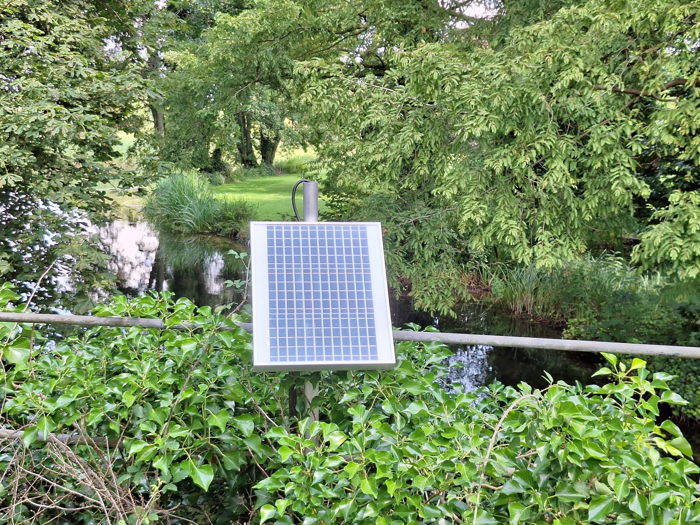 A river water quality monitoring panel surrounded by trees and greenery