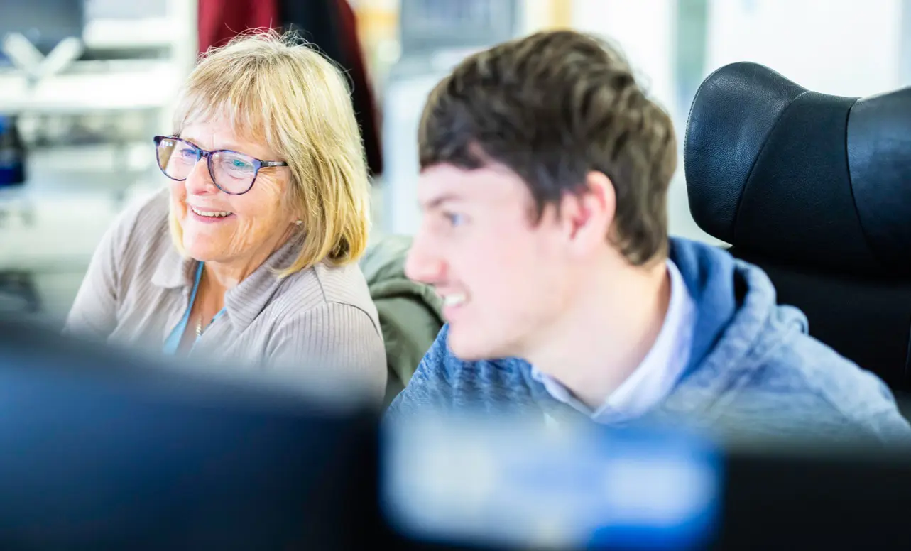 A close up shot of two people conversing while looking at computer monitors