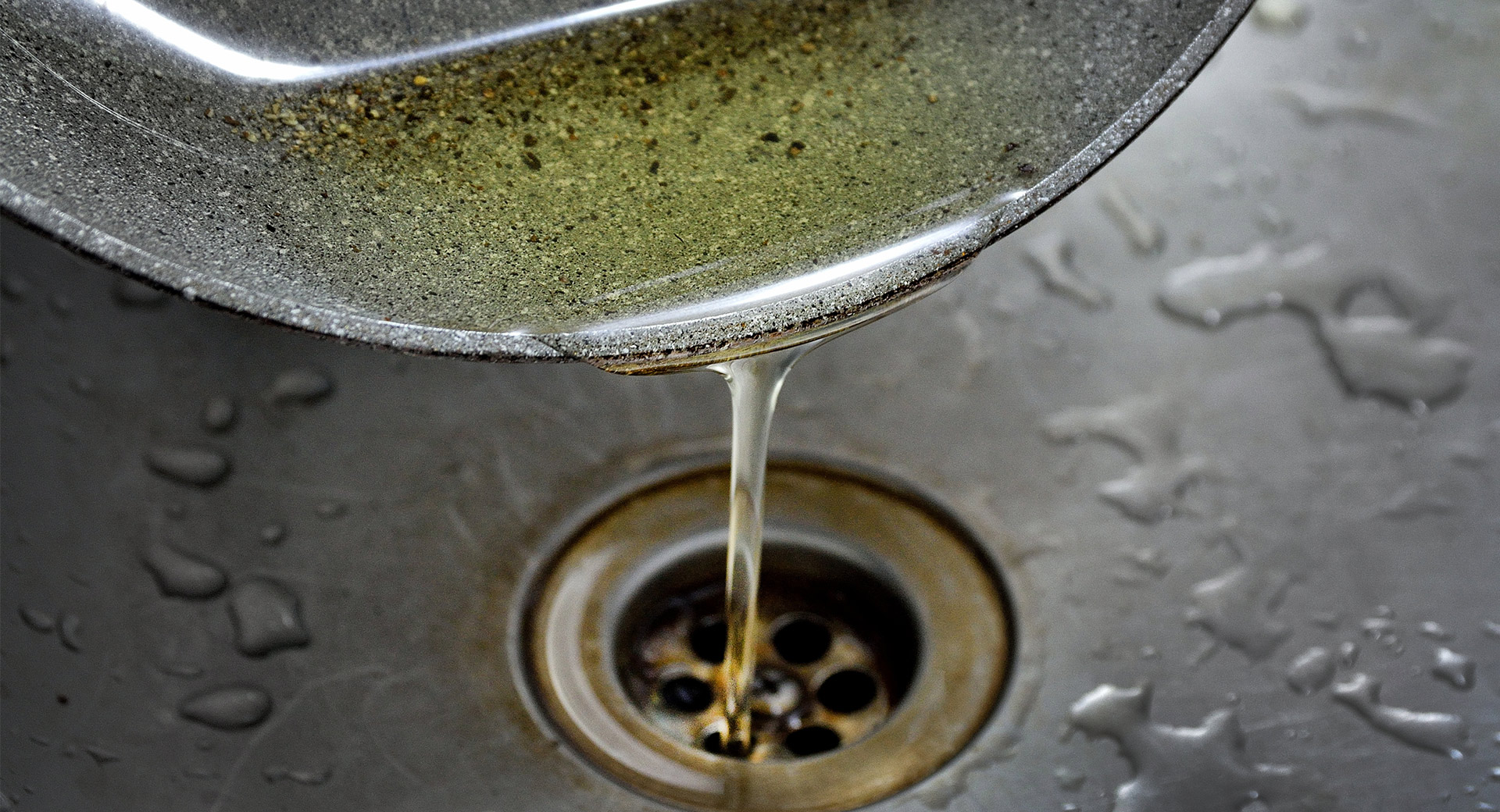 A person pouring oil down a sink
                        