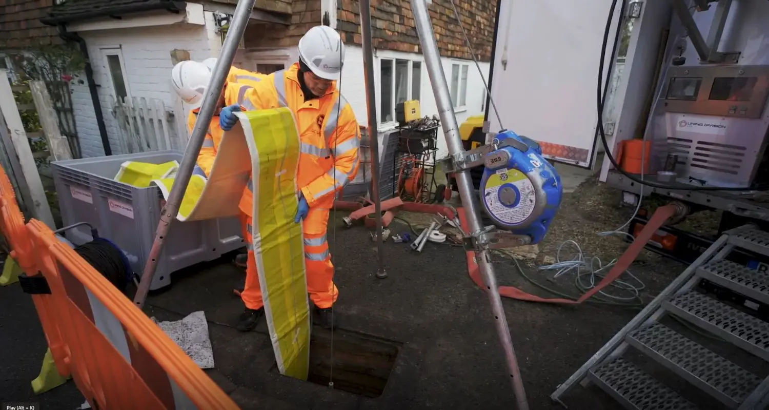 man lowering new sewer lining into the ground